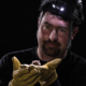 A helmeted biology professor Tim Carter holds a small bat in the palm of his hands.
