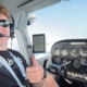 Luke Dalton sits in a cockpit in sunglasses taking a selfie with a thumbs up.