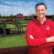 Mike Shebek stands in front of the Shebek Stadium with his arms crossed in a red Ball State pullover.