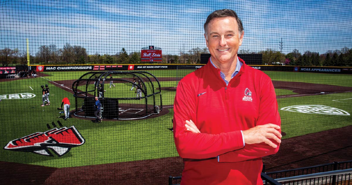 Mike Shebek stands in front of the Shebek Stadium with his arms crossed in a red Ball State pullover.
