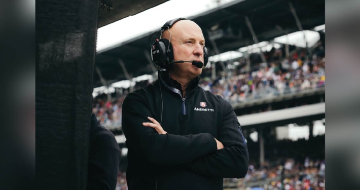 Dan Towriss stands with his arms crossed wearing a headset inside a stadium.