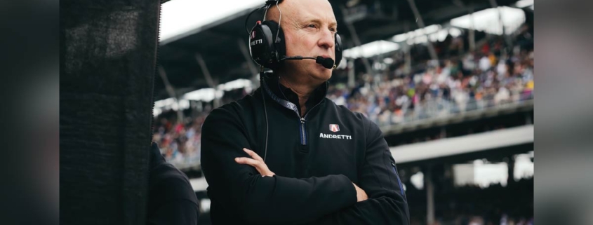 Dan Towriss stands with his arms crossed wearing a headset inside a stadium.