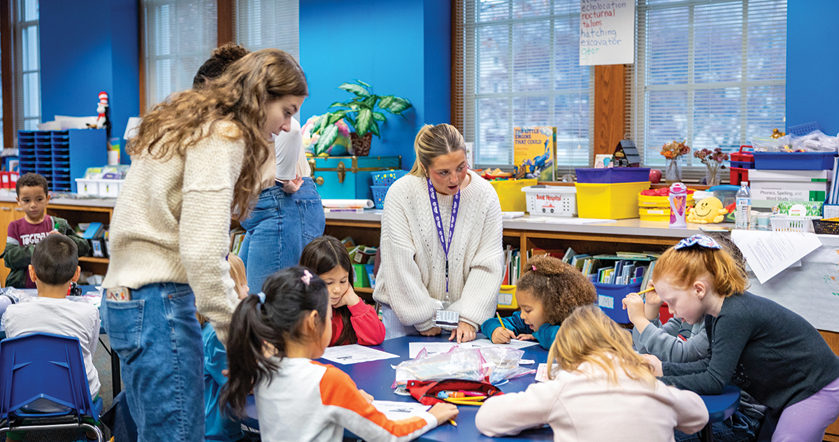 Teachers assist young Burris students with classroom activities around a table in a classroom.