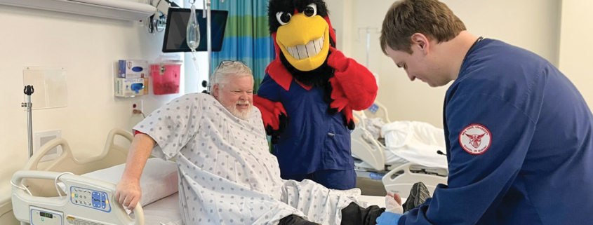 Person on bed with ankle wrapped, Charlie cardinal in background and nursing student tending to ankle
