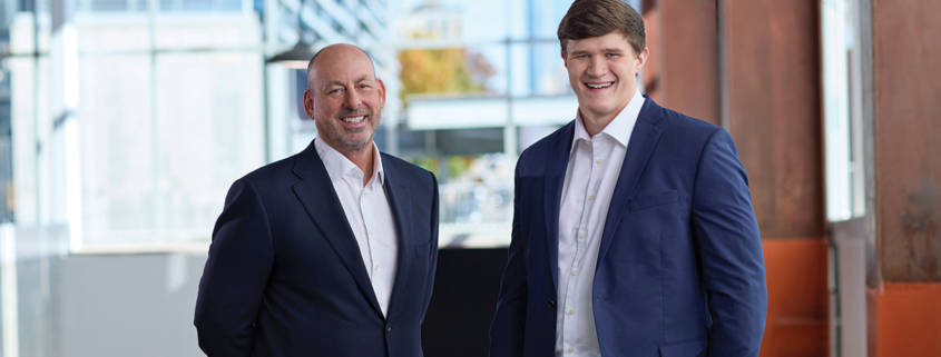 Lou Hensley (left) and Caleb Murray (right), both smiling and dressed in suits.