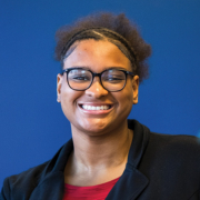 Janiya Milton, smiling and wearing a black blazer with a red undershirt.