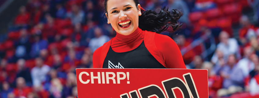 A Ball State cheerleader smiles while holding a sign that reads "Chirp! Chirp!"