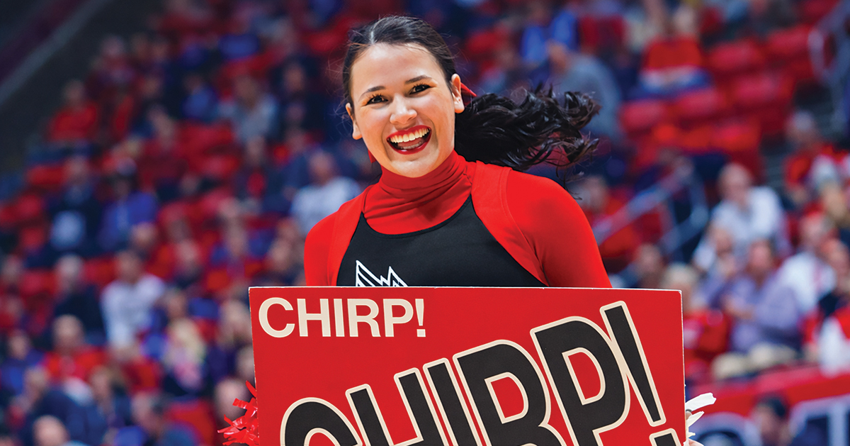 A Ball State cheerleader smiles while holding a sign that reads 