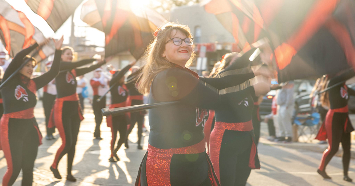 A Ball State color guard member smiles and twirls a flag during a parade.
