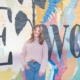 Woman standing in front a wall mural that says "Elwood"