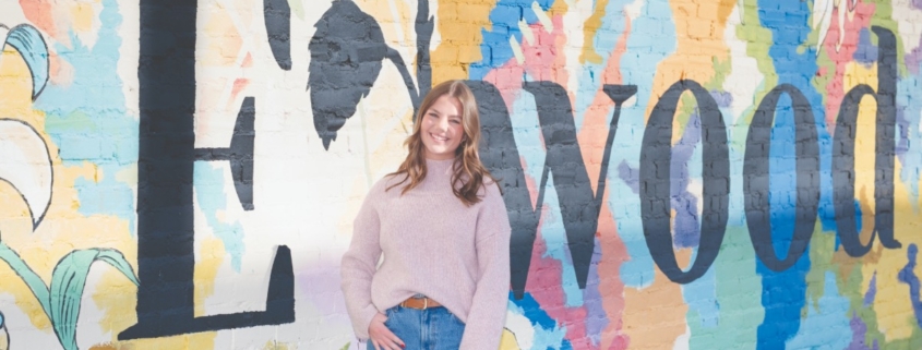 Woman standing in front a wall mural that says "Elwood"