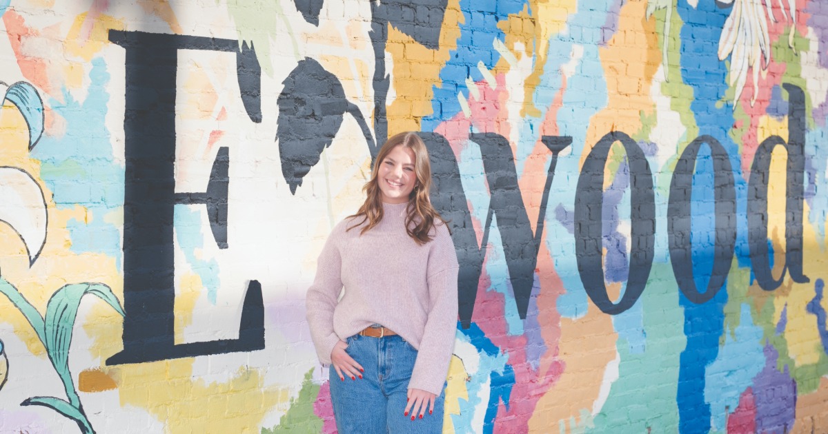Woman standing in front a wall mural that says 