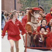 Students push anded bed down the road with two mascots riding on it.