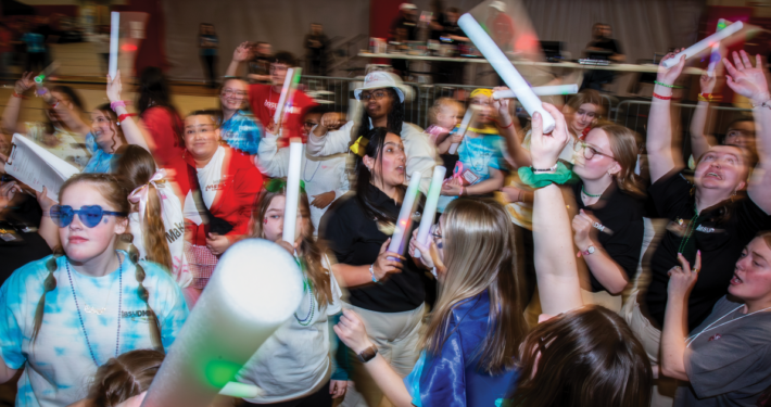 A road of young adults dance with glow sticks.