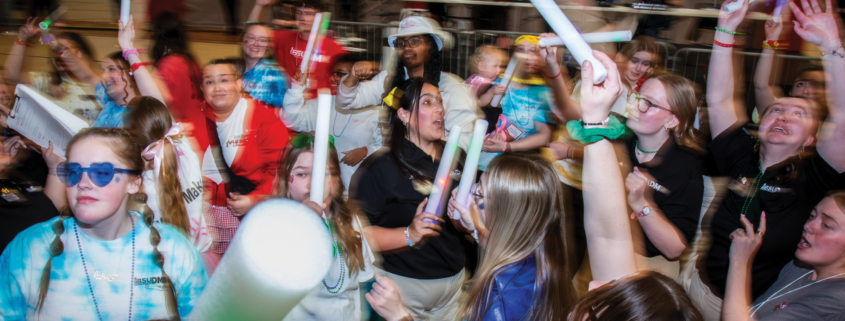 A road of young adults dance with glow sticks.