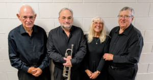 Four people pose together wearing black and one holds a trumpet.