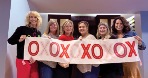 Women stand together holding a banner that says "OXOXOXOXOX"