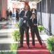 Two people stand on a red carpet and pose together