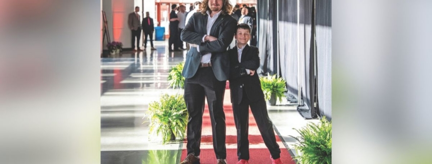 Two people stand on a red carpet and pose together