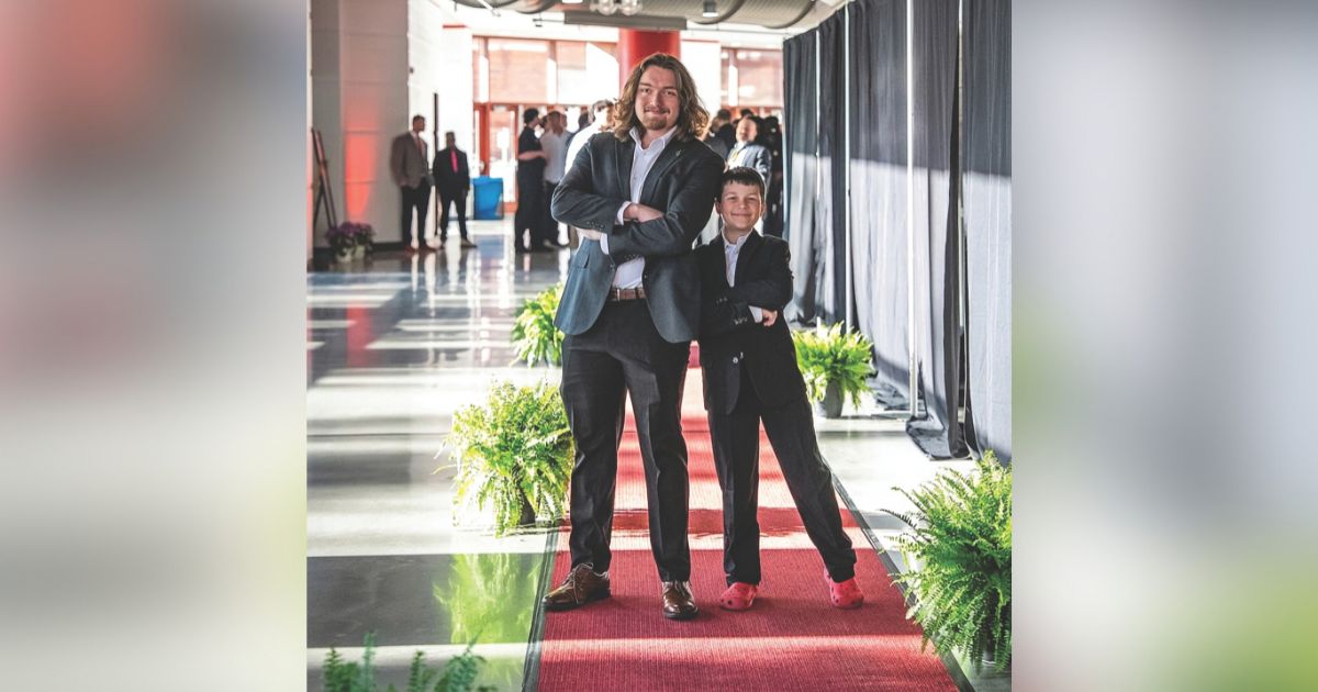 Two people stand on a red carpet and pose together