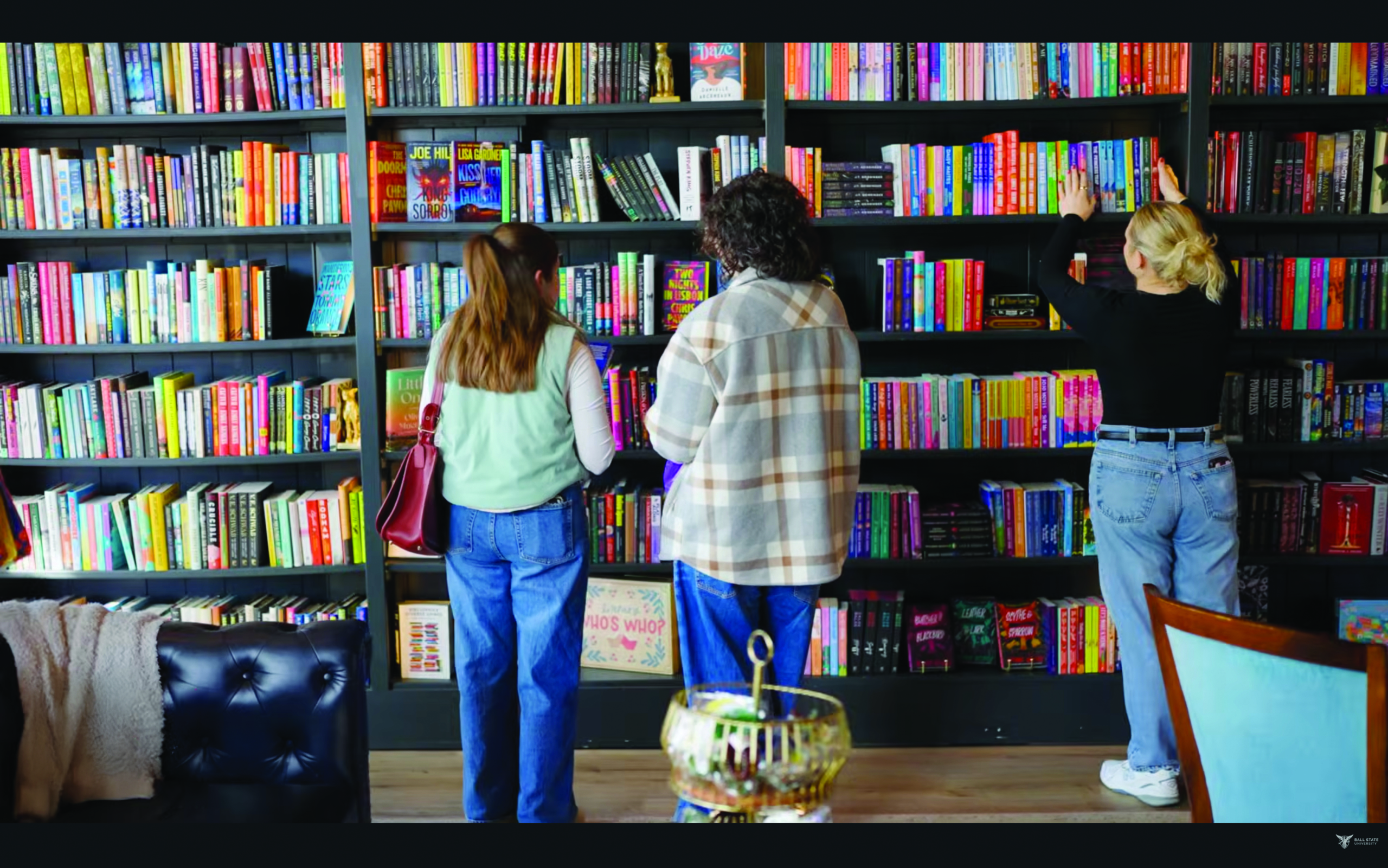 Lounge full of books on a shelf with three people standing in front with their backs turned