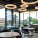Modern lounge and collaboration space with tables, seating, large windows, and circular ceiling lights overlooking the Ball State campus.