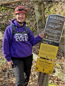 A woman poses next to a sign warning for bats.