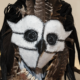 Elaborate owl-inspired costume made with feathers, fabric, and a white-and-black face covering, displayed in a museum gallery.